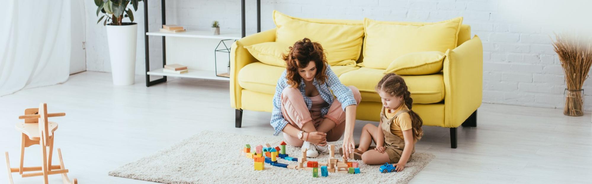 Nanny and kid are playing with toys on the floor.